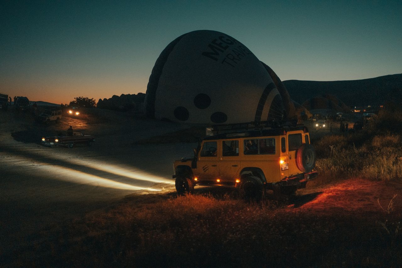 Yellow jeep parked at dusk beside a hot air balloon, creating a serene evening scene.