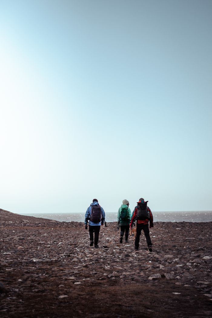 Three adventurers hiking on a rocky coastline, showcasing outdoor exploration and travel.